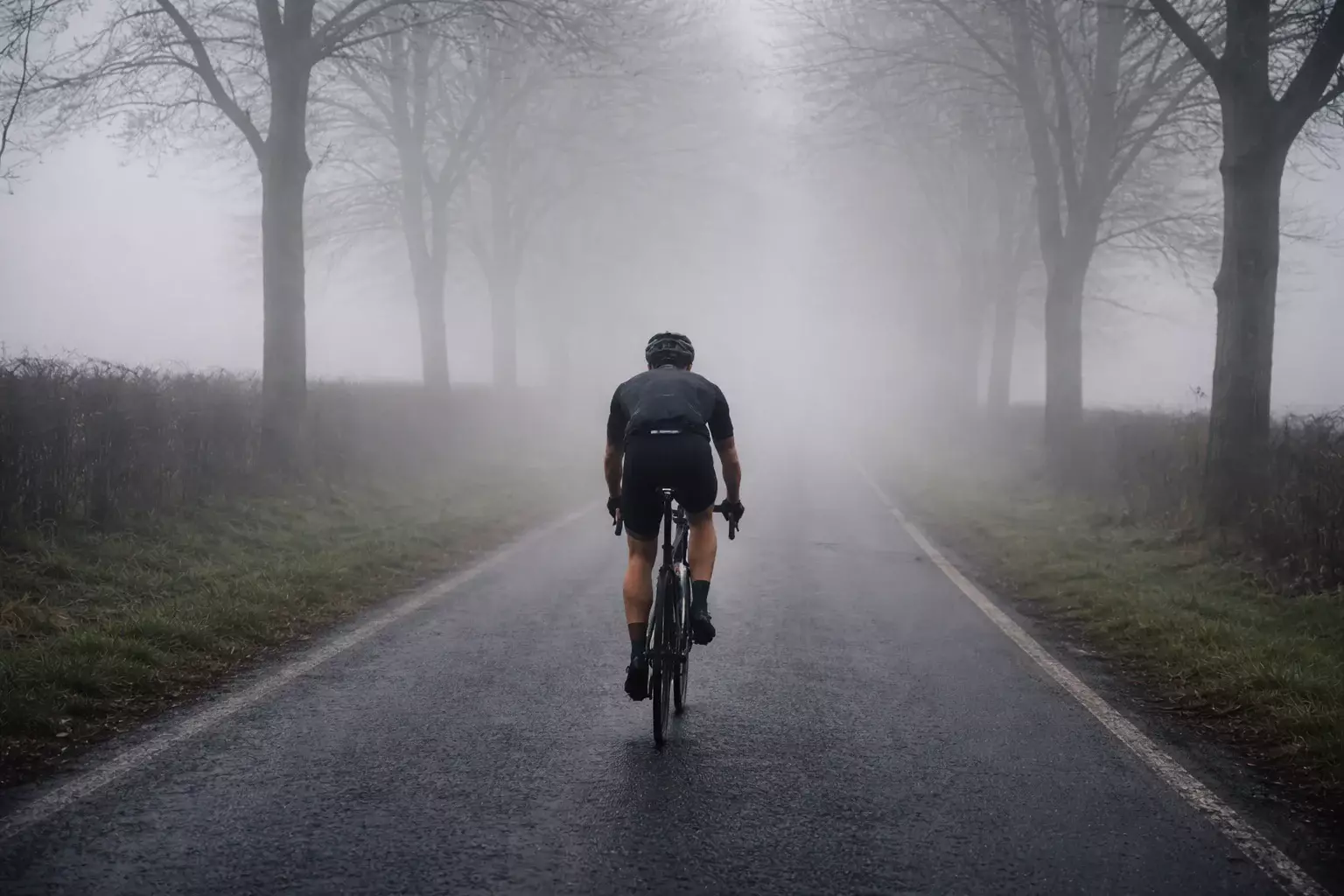 Cycliste professionnel seul sur une route de campagne brumeuse symbolisant l'incertitude des pronostics sportifs